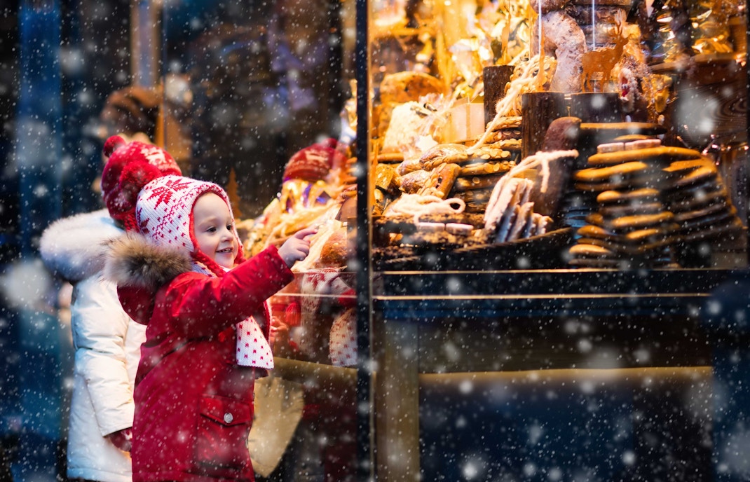 Child admiring holiday treats in a snowy Orlando Christmas market.