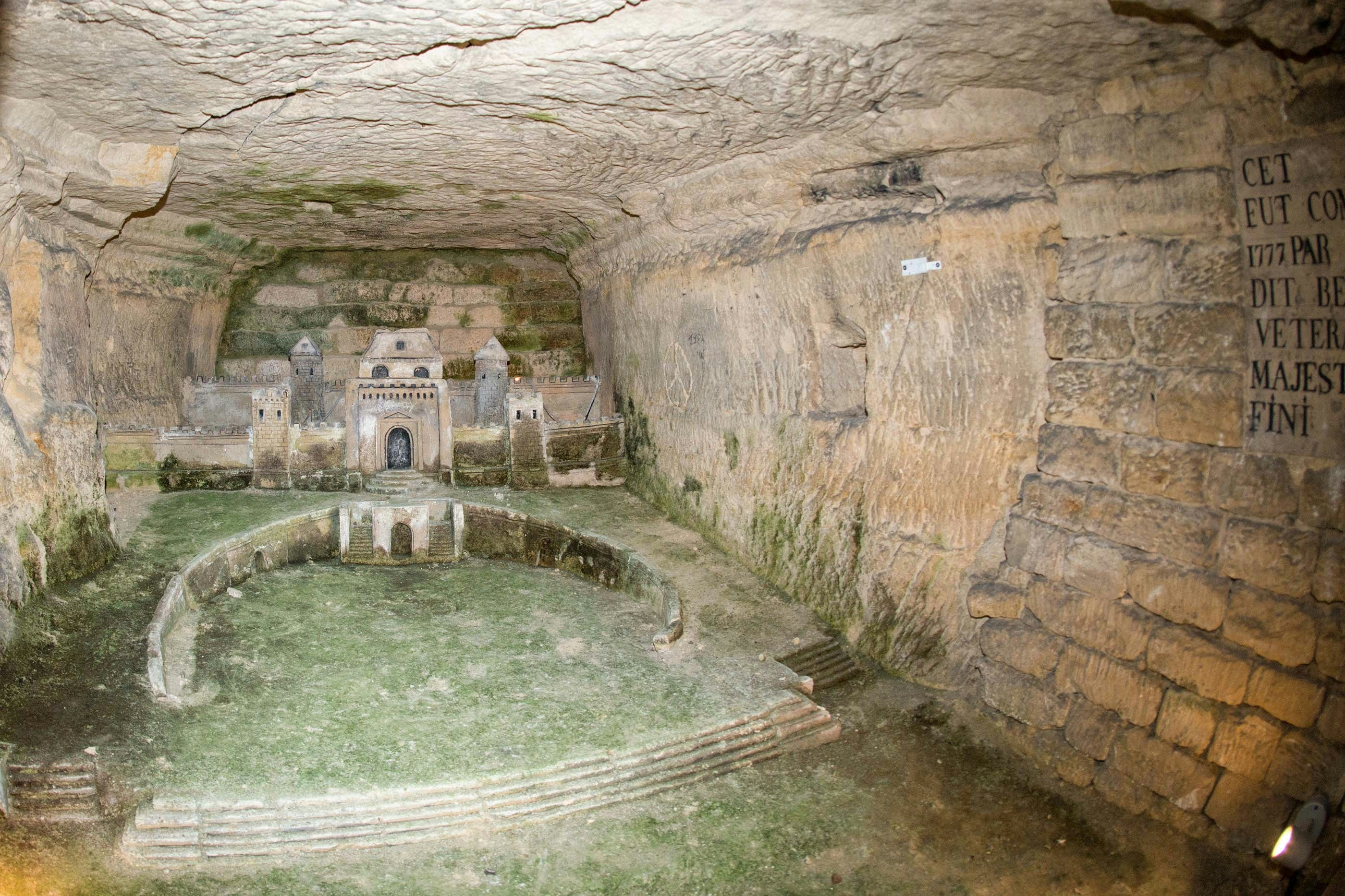 Port Mahon model in Paris Catacombs corridor, showcasing intricate stone carvings.