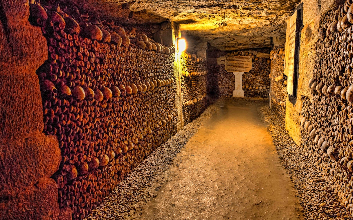 Catacombs of Paris with skull-lined walls, illuminated passageway.