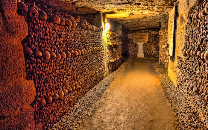 Catacombs of Paris with skull-lined walls, illuminated passageway.