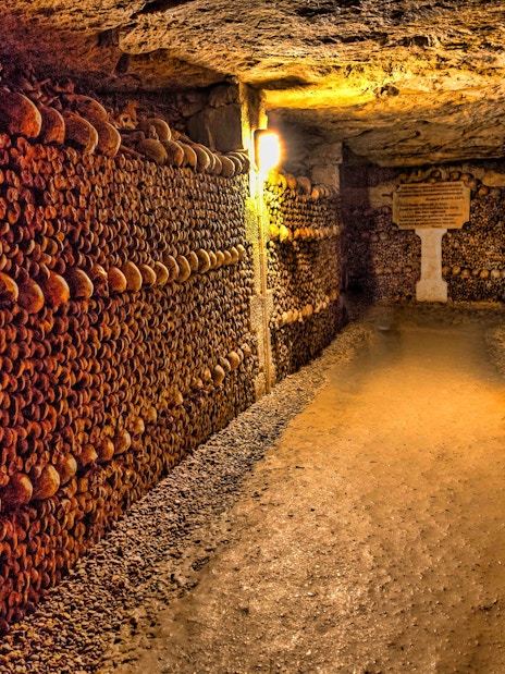 Catacombs of Paris with skull-lined walls, illuminated passageway.