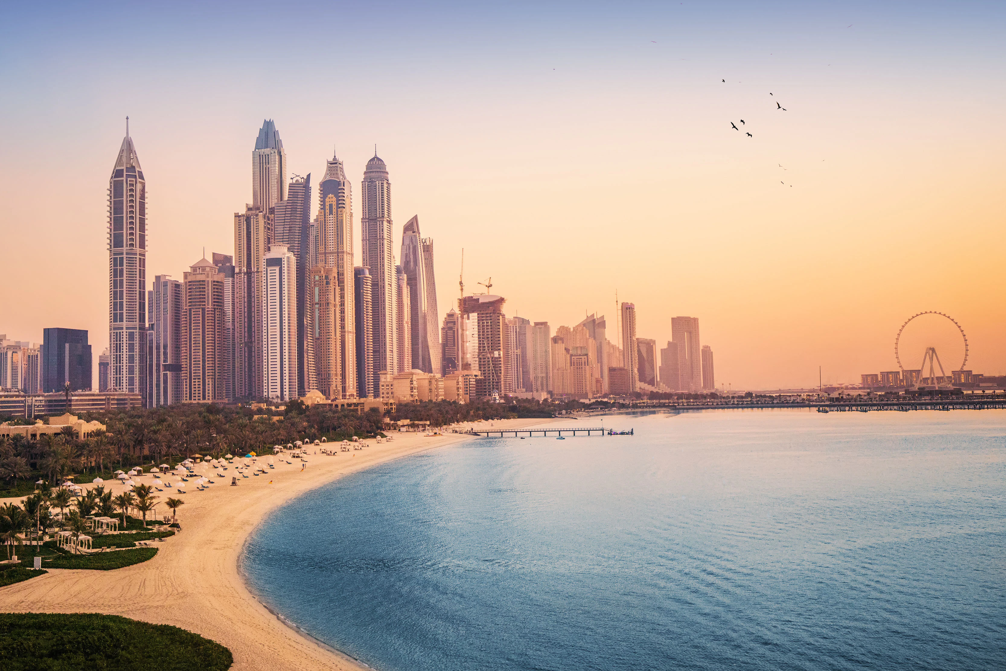 Dubai Marina skyline and JBR Walk at sunset with beach and Ferris wheel.