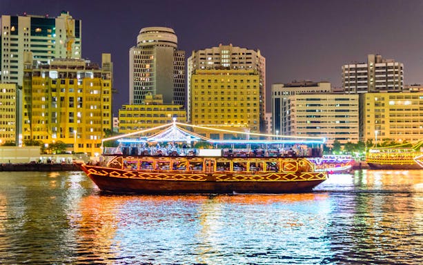 Dhow cruise on Dubai Creek with city skyline at night.