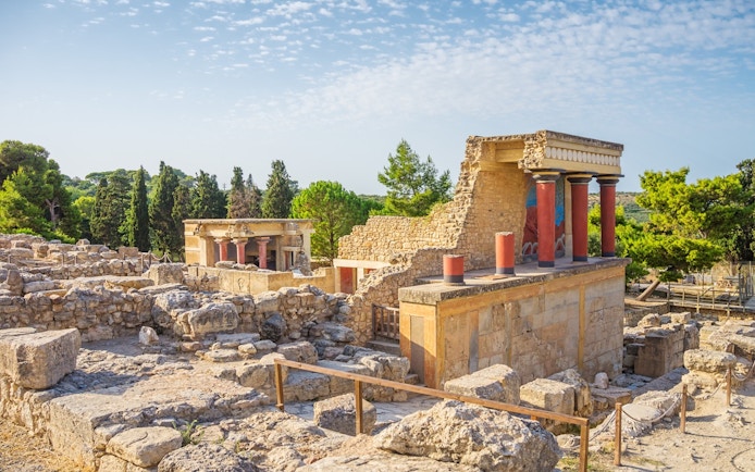 Knossos Palace ruins with red columns and ancient stone structures in Crete, Greece.