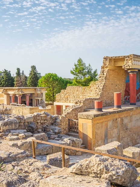 Knossos Palace ruins with red columns and ancient stone structures in Crete, Greece.