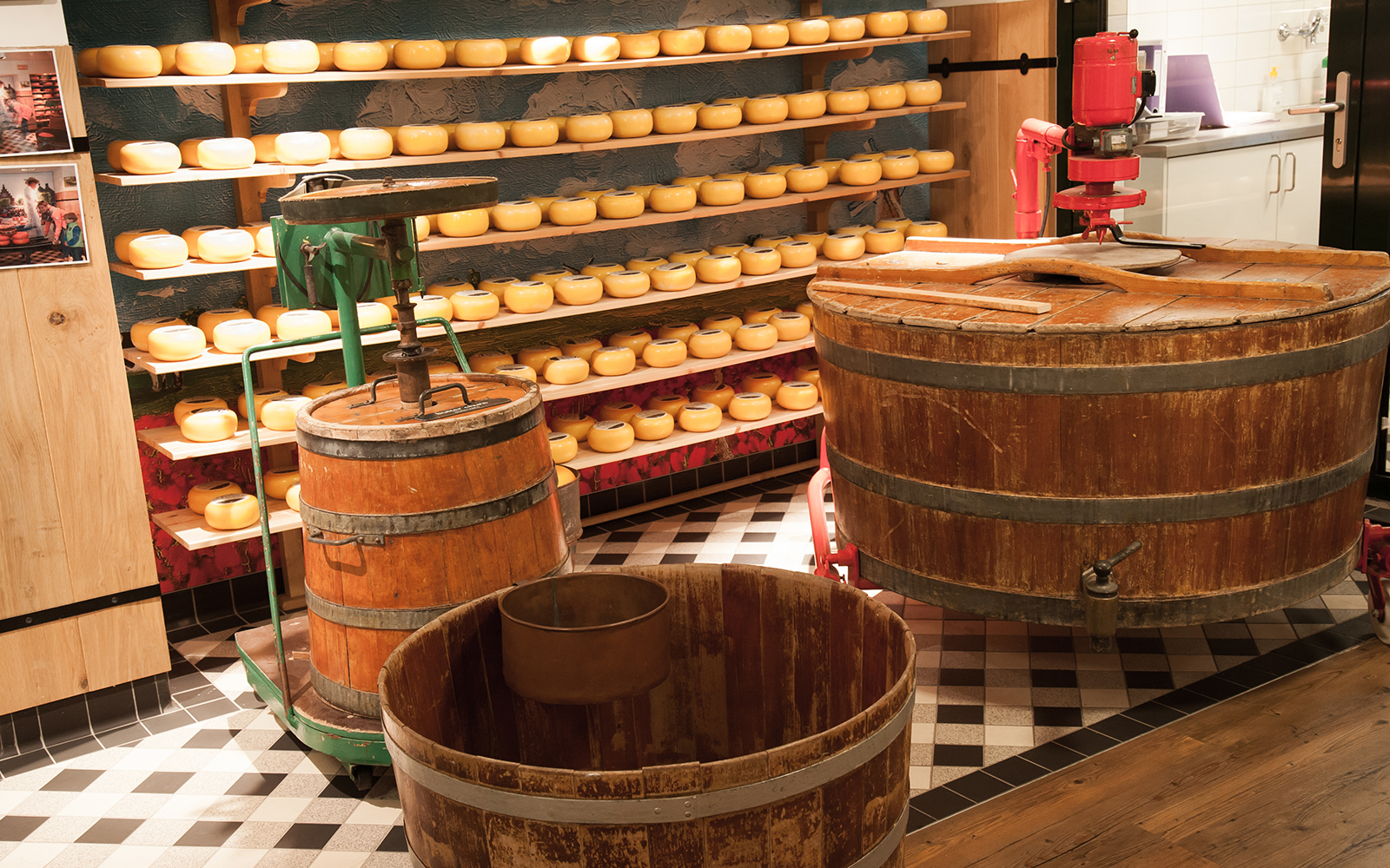 Cheese wheels aging on shelves at Volendam Cheese Factory with wooden vats in foreground.