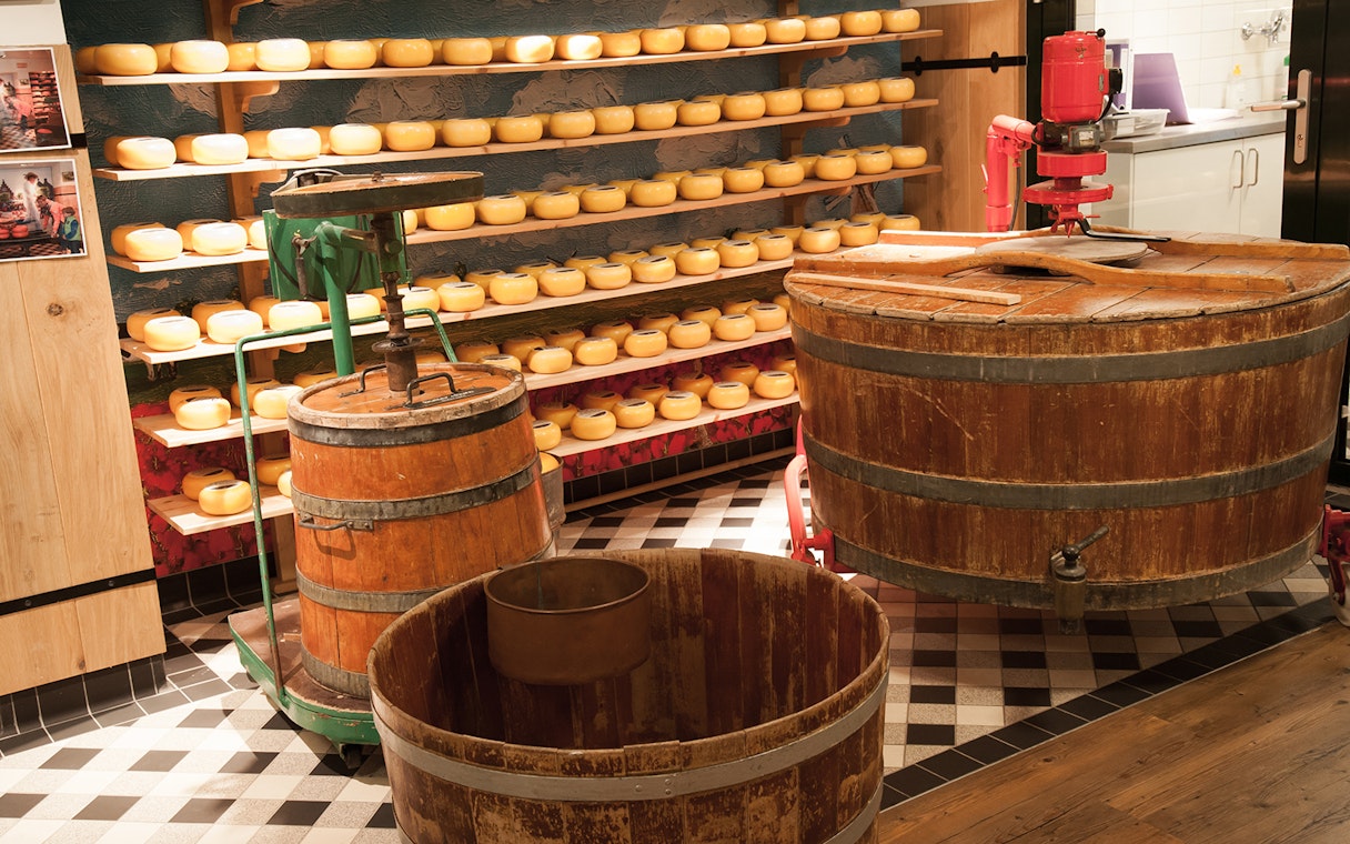 Volendam cheese factory interior with cheese wheels and visitors exploring production process.