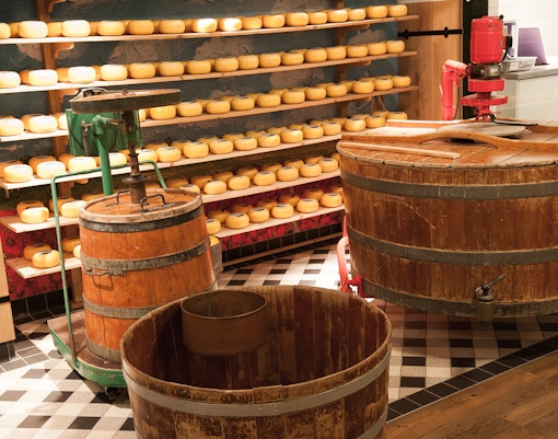 Volendam cheese factory interior with cheese wheels and visitors exploring production process.