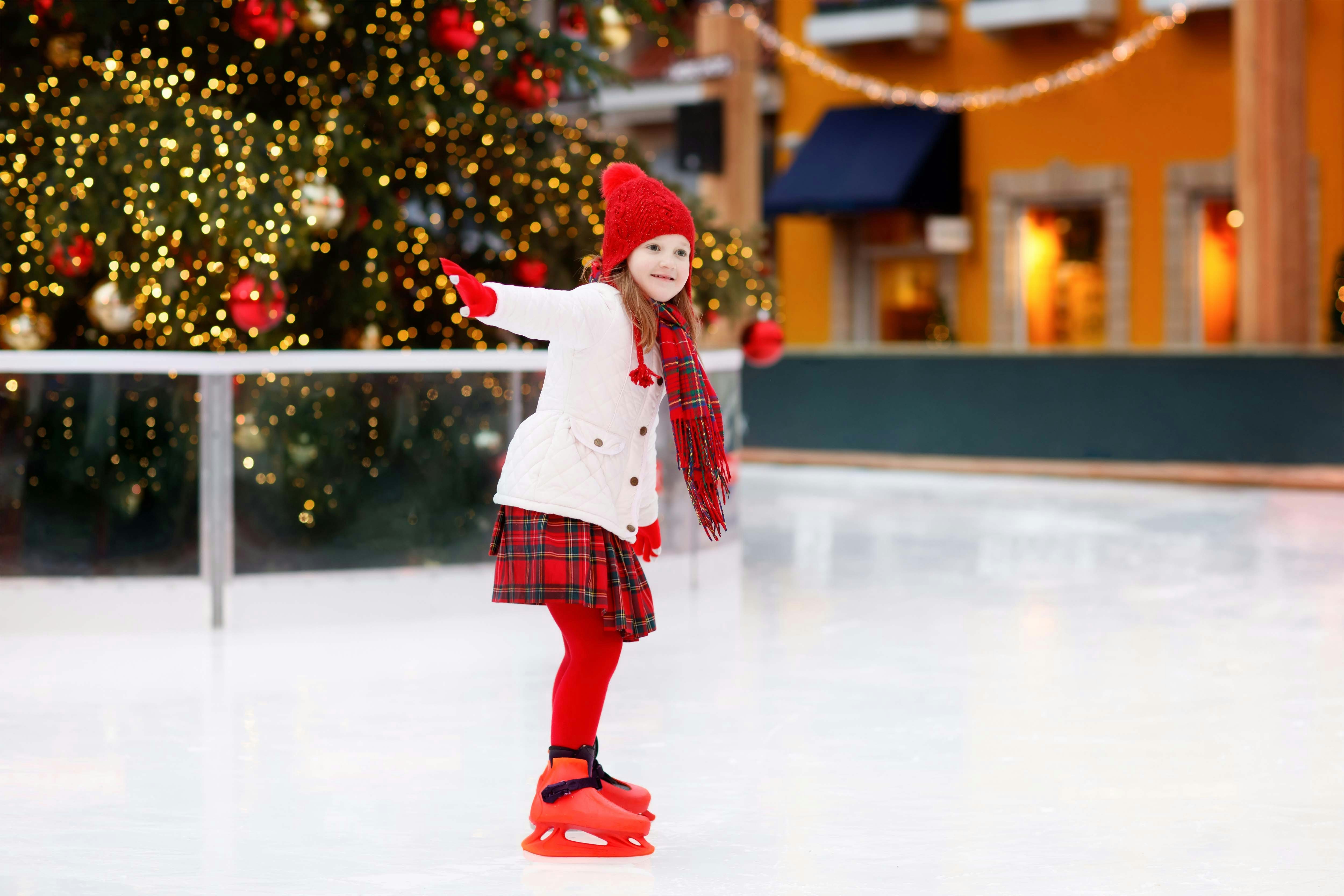 Child ice skating in Amsterdam with Christmas lights and tree in the background.
