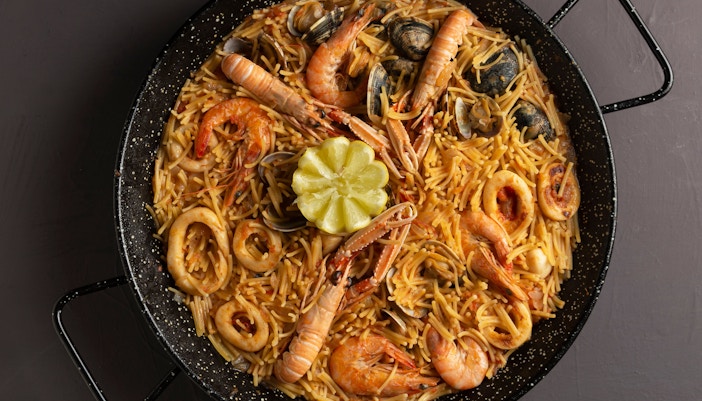 Fideuà dish with seafood and lemon wedges, Barcelona food guide.