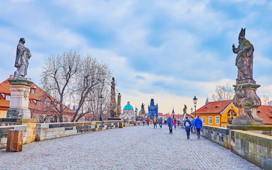 Tour group crossing Charles Bridge towards Prague Castle with Old Town in the background during Christmas.