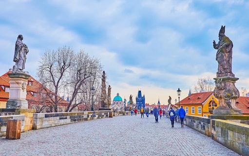 Tour group crossing Charles Bridge towards Prague Castle with Old Town in the background during Christmas.
