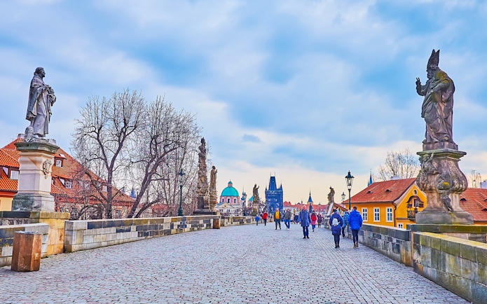 Tour group crossing Charles Bridge towards Prague Castle with Old Town in the background during Christmas.