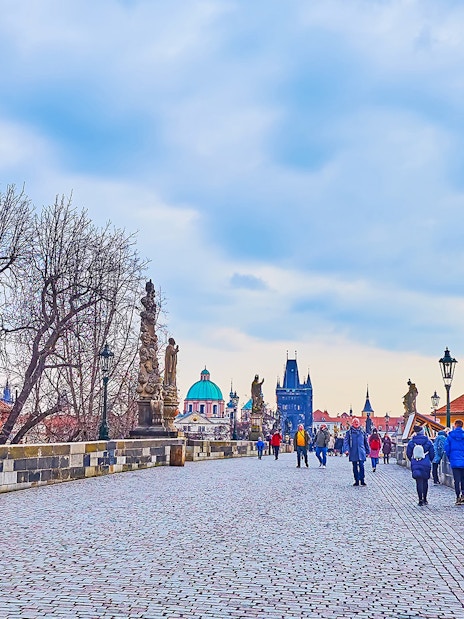 Tour group crossing Charles Bridge towards Prague Castle with Old Town in the background during Christmas.