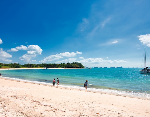 Beach scene with people walking along the shore and a sailboat in the water at St. John's Island.