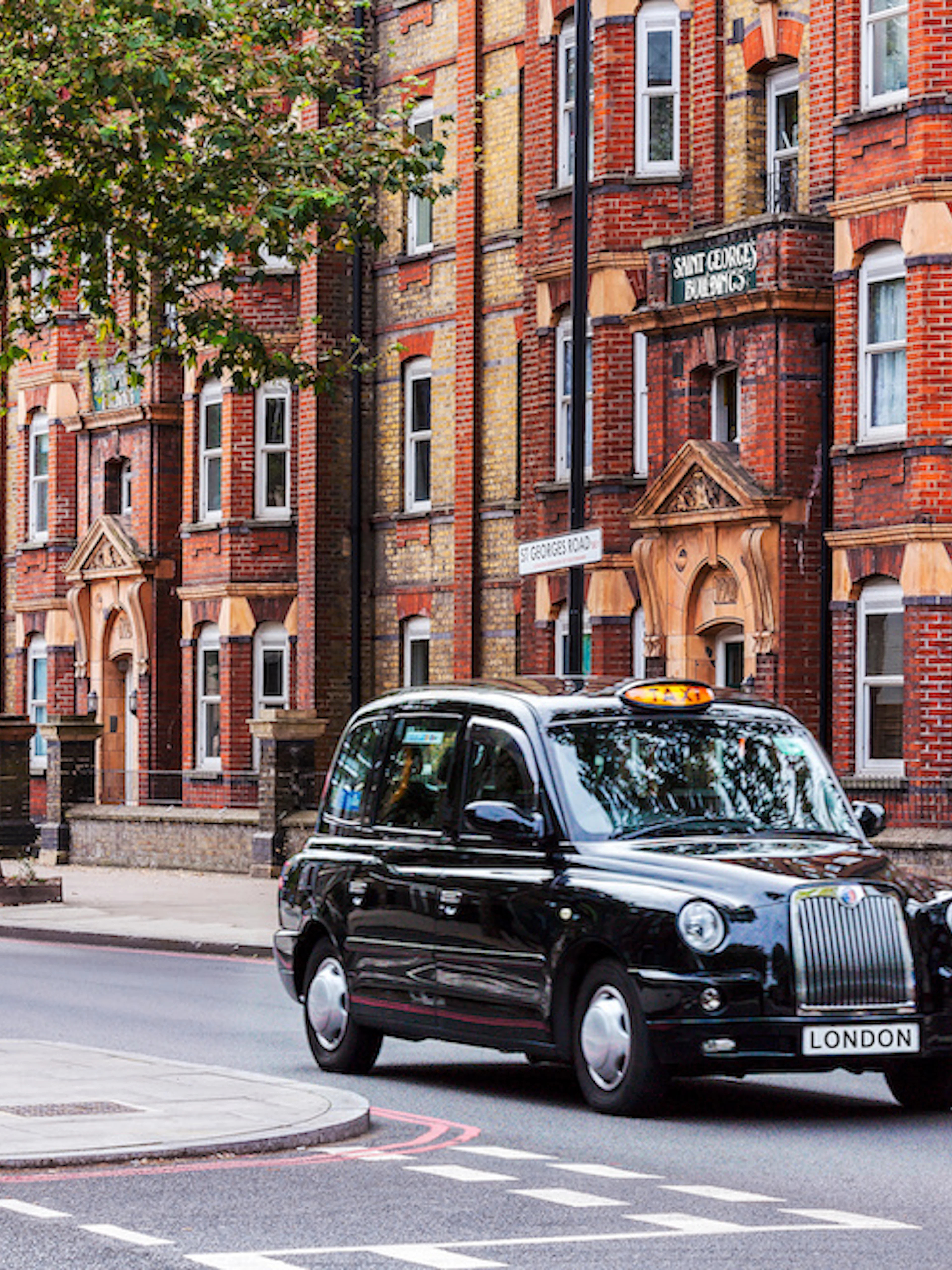 Black taxi driving on a London street with historic buildings in the background.