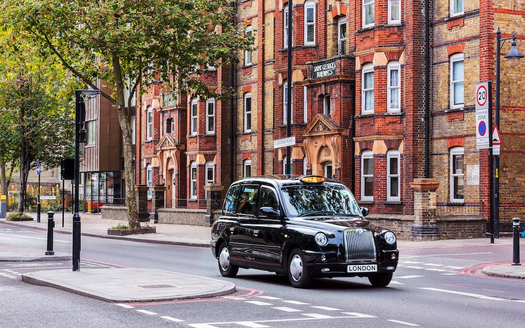 Black taxi driving on a London street with historic buildings in the background.