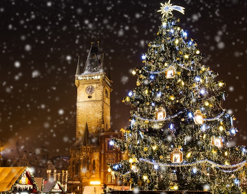 Christmas tree and Old Town Tower in Prague with falling snow.