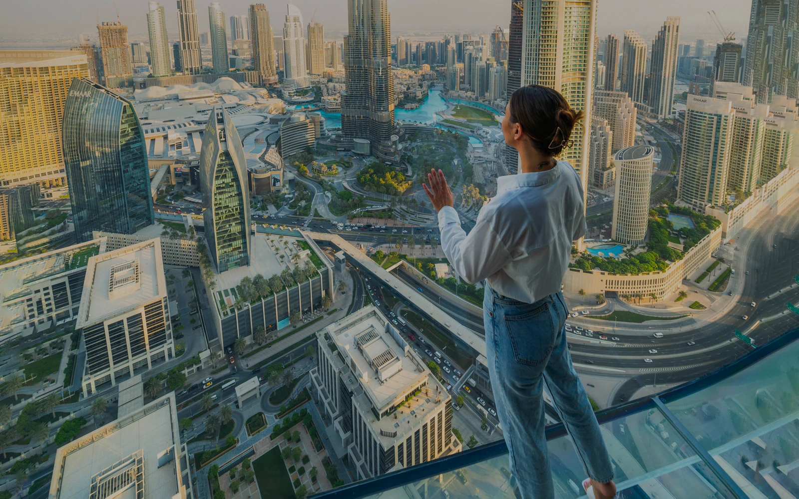 Person standing on a glass slide overlooking Dubai skyline.