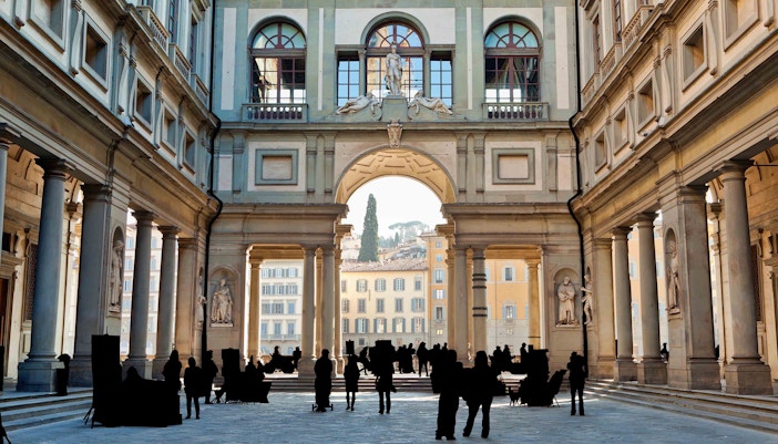 Silhouettes of tourists standing in the majestic entrance of the Uffizi Gallery, with sculptures adorning the arcade, inviting exploration