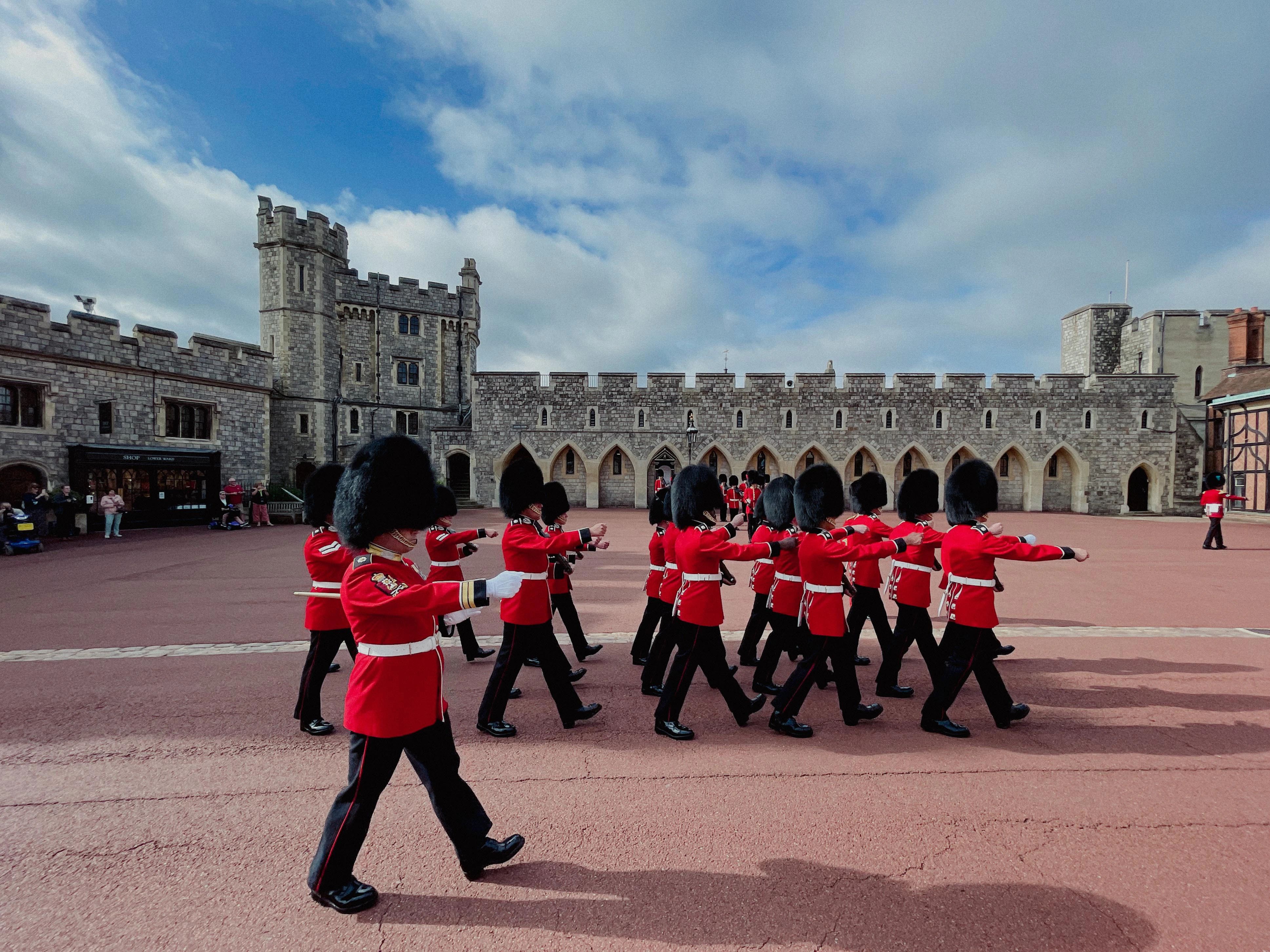 Guards in red uniforms marching at Windsor Castle courtyard, England.
