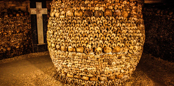 Barrel of bones in Paris Catacombs with cross in background.