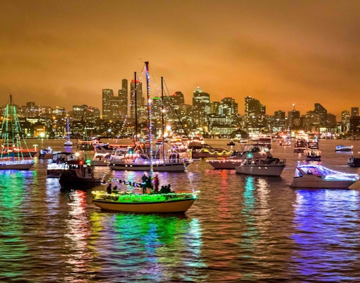 Boats adorned with Christmas lights in an Orlando parade against a city skyline.