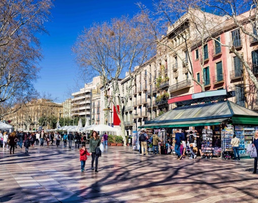 Crowded street scene on La Rambla, Barcelona, with kiosks and historic buildings.