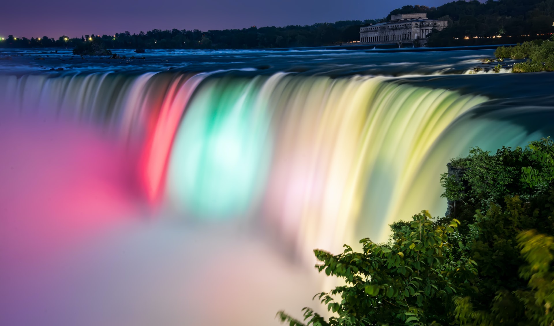 Niagara Falls illuminated at night with colorful lights, view from New York side.