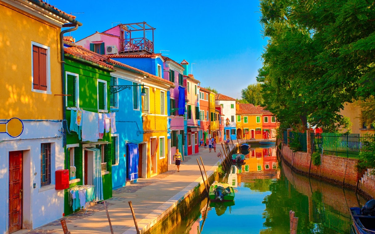 Tourists walking along the colorful houses of Burano, Venice, near a canal.