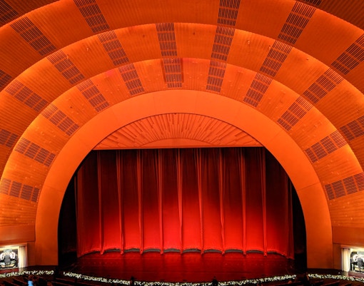 Radio City Music Hall stage with iconic red curtains and grand auditorium seating.