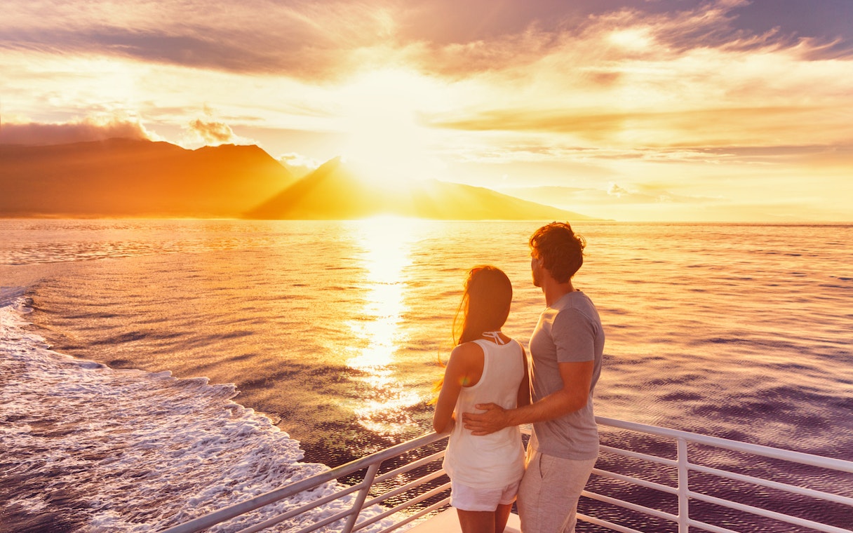 Couple enjoying sunset on a sailing cruise with ocean and mountains in view.