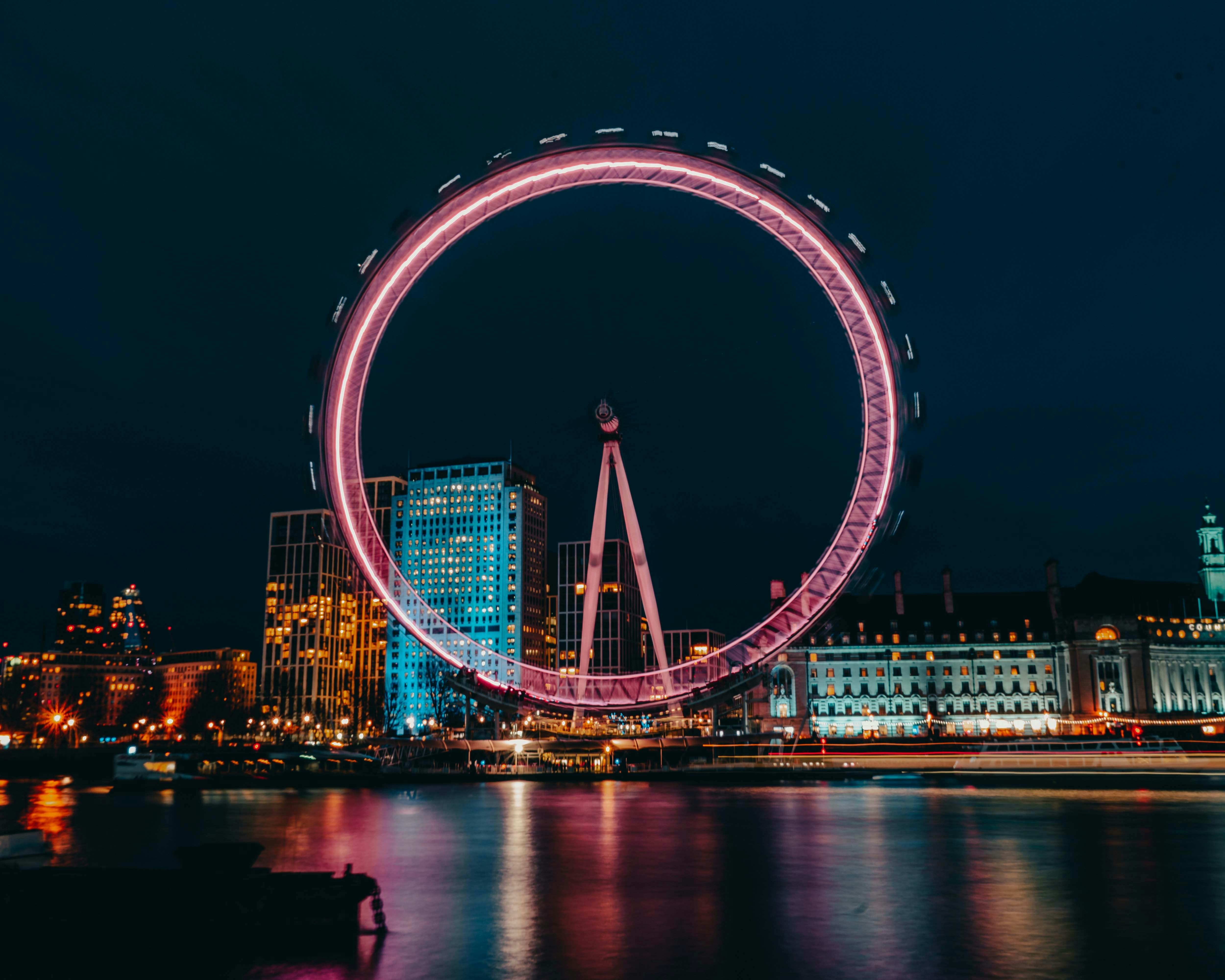 London Eye illuminated at night with city skyline in the background.