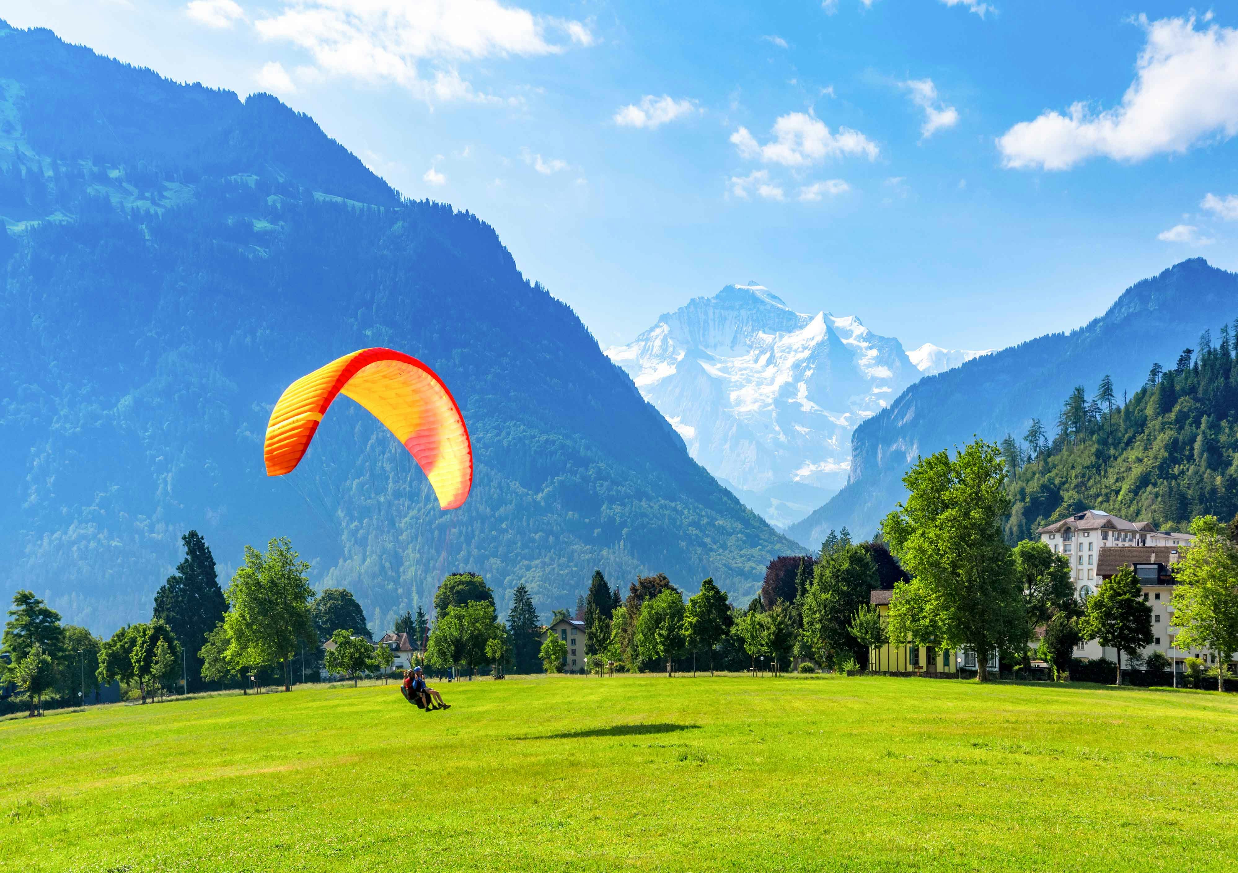 Paragliding over green fields with mountains in Interlaken, Switzerland.