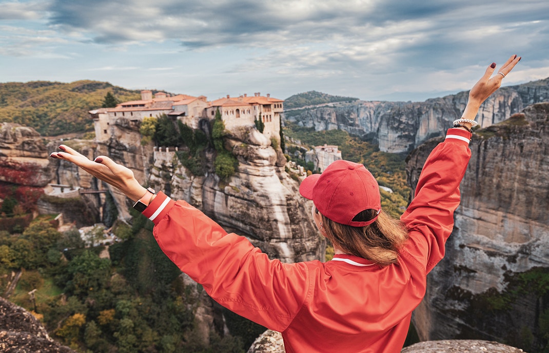 Person admiring Meteora monasteries from a cliff, Greece, during a hiking tour.