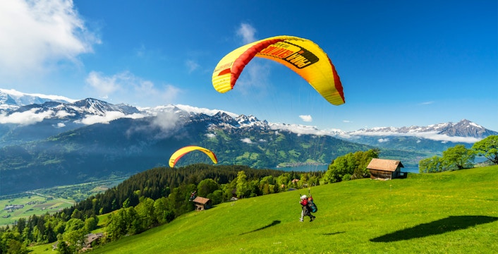 Paragliders soaring over green hills with snow-capped mountains in Interlaken, Switzerland.