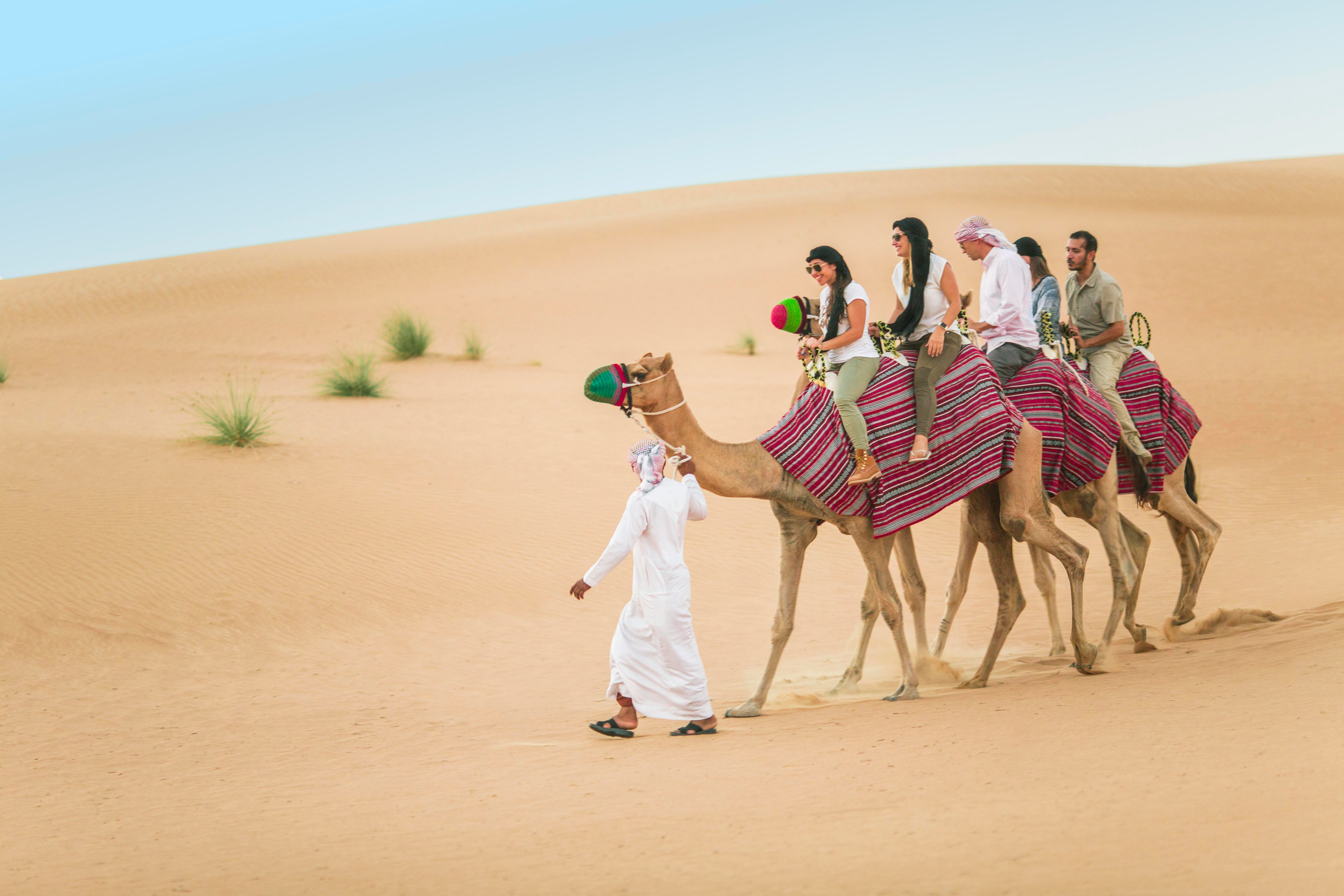 Camel ride in Dubai desert safari with tourists on sand dunes.