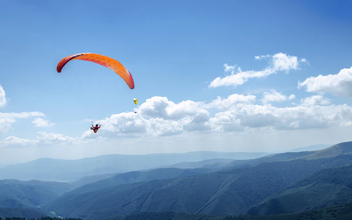 Skydiver with orange parachute over mountains in Wollongong, Sydney.