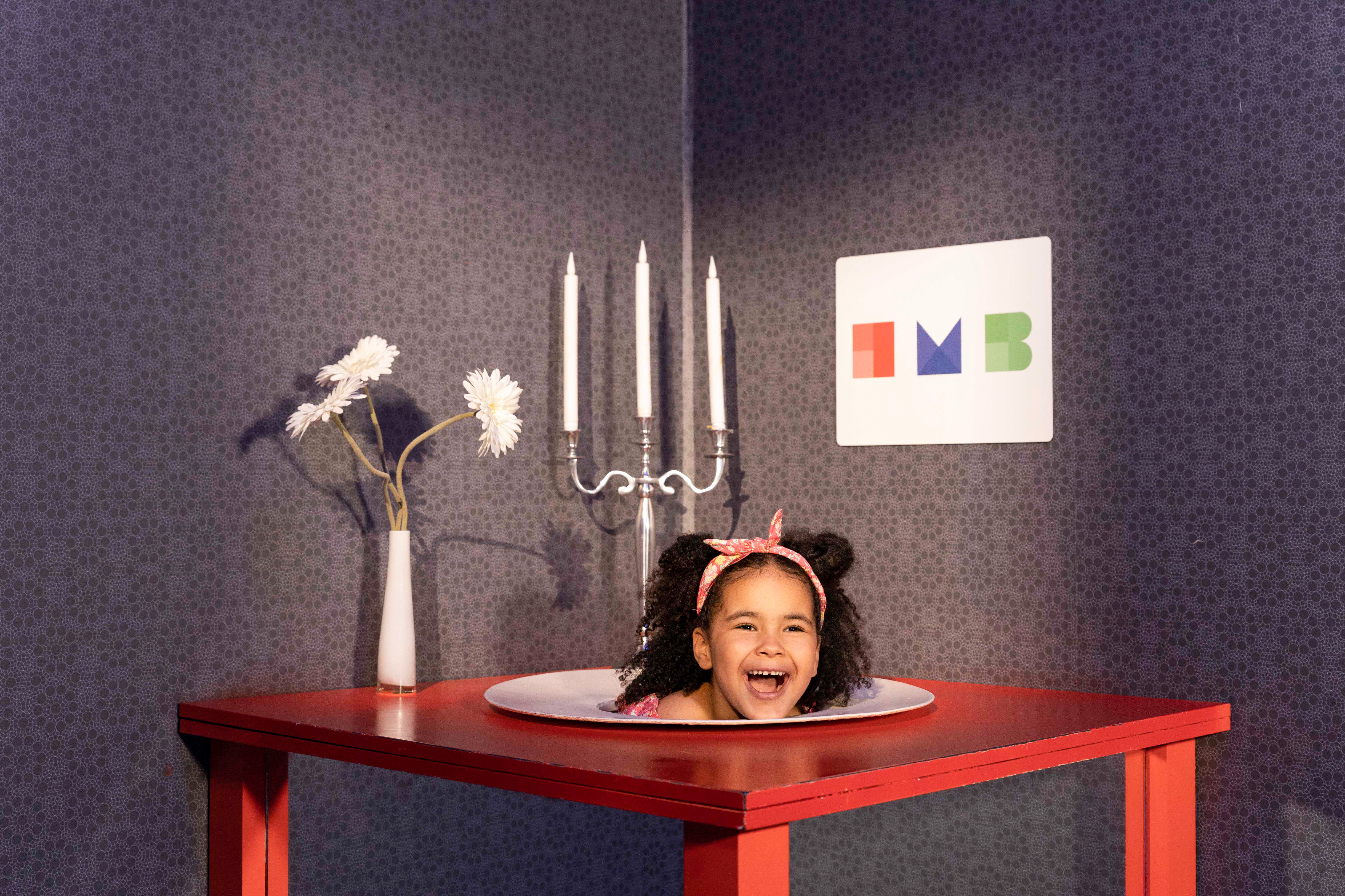 Ein Tisch mit Blumenvase und Kerzenständer und einem Teller, auf dem der Kopf eines Kindes zu liegen scheint