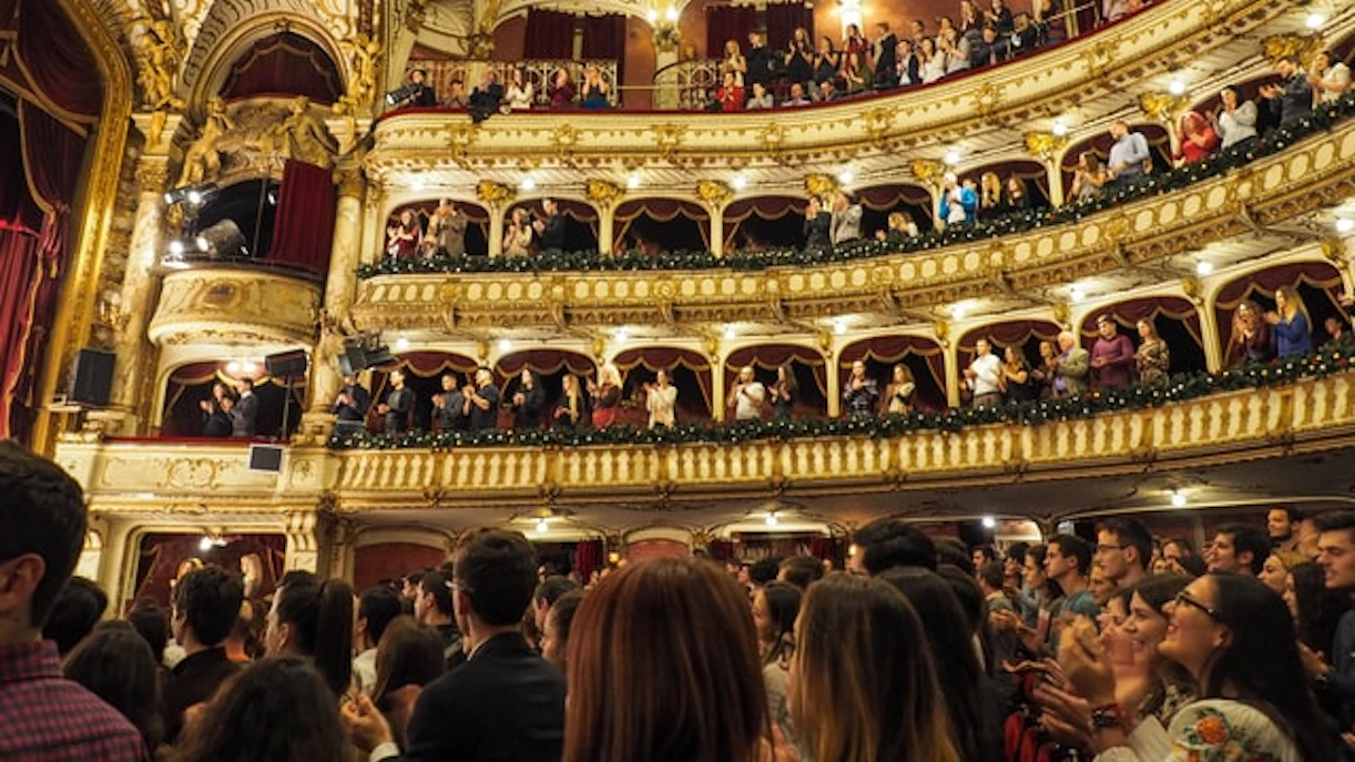 Audience applauding in a grand theater with ornate balconies.