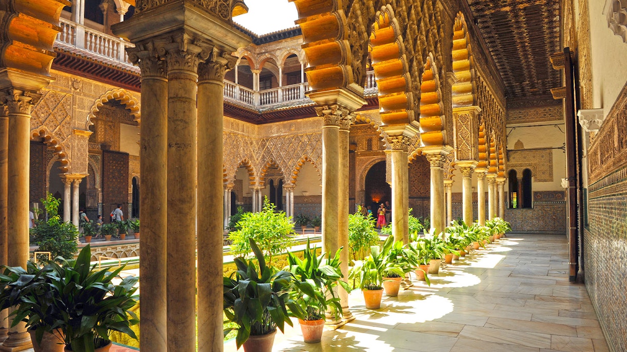 Alcazar of Seville courtyard with intricate arches and lush gardens.