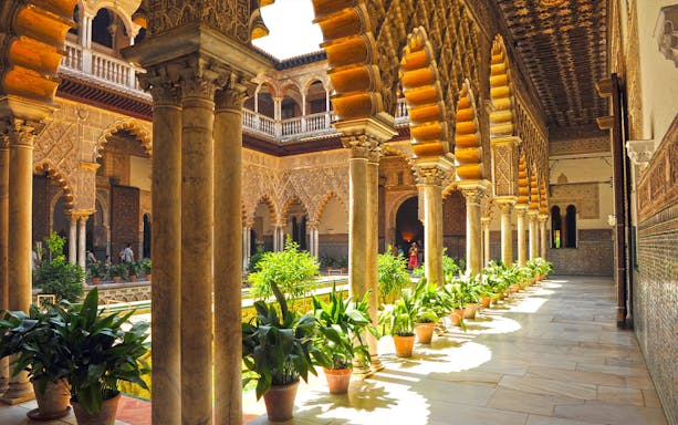 Alcazar of Seville courtyard with intricate arches and lush gardens.
