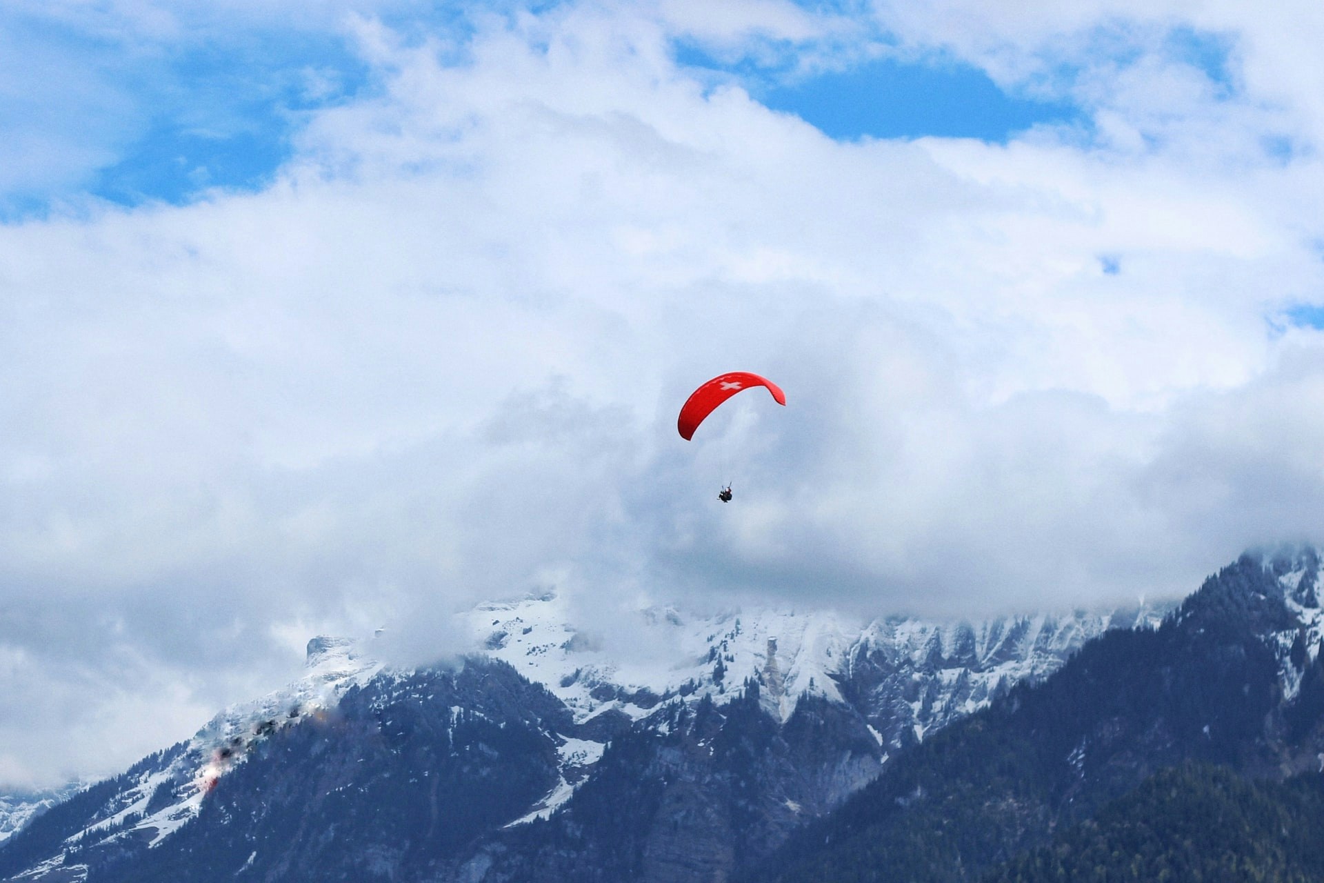 Paraglider soaring over snowy mountains in Interlaken, Switzerland.