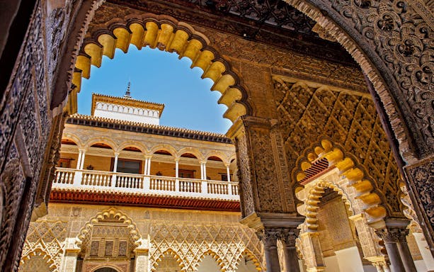 Alcazar of Seville courtyard with intricate arches and reflecting pool.