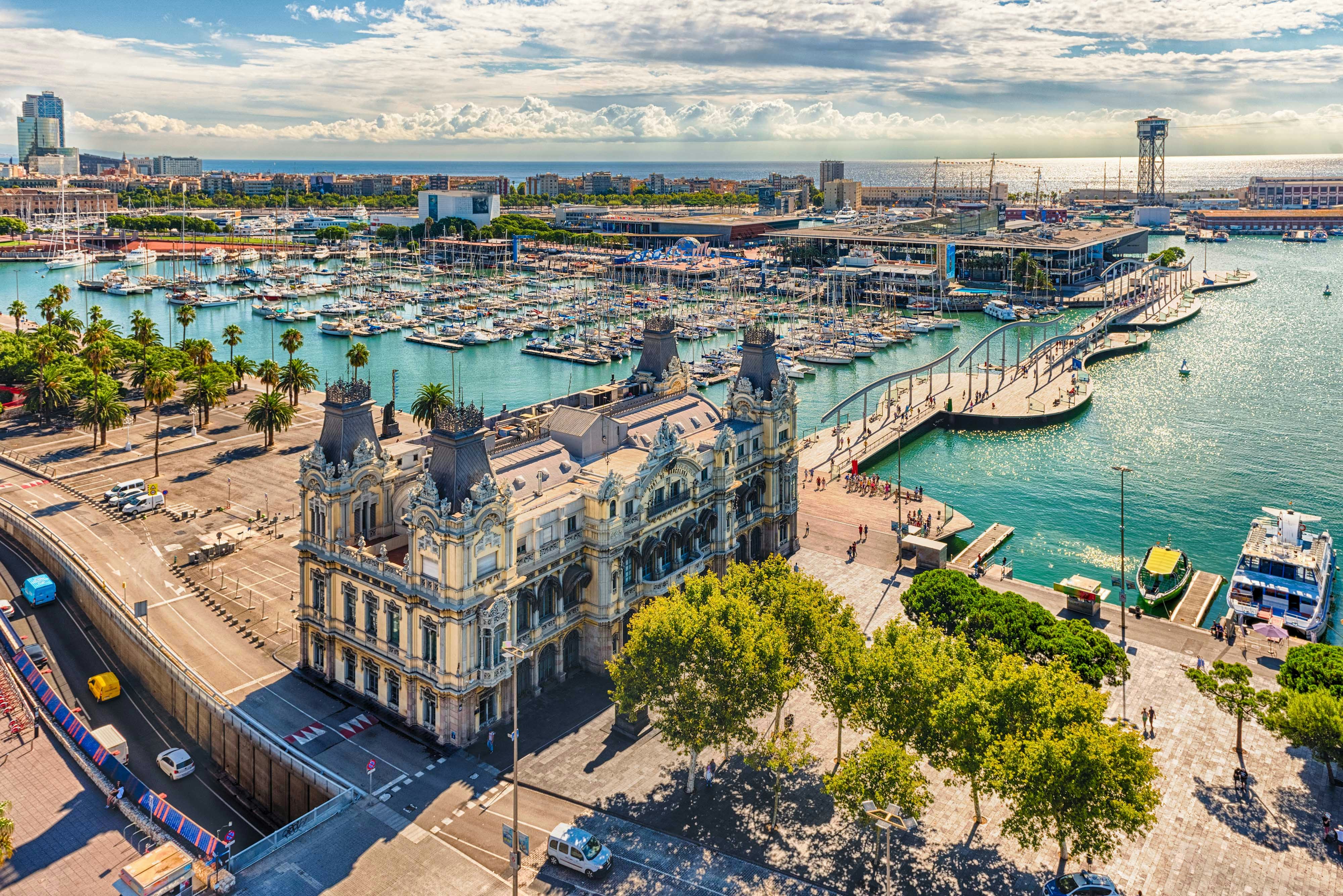 Barcelona Hop-on Hop-off bus at Port Vell with marina and cityscape in the background.