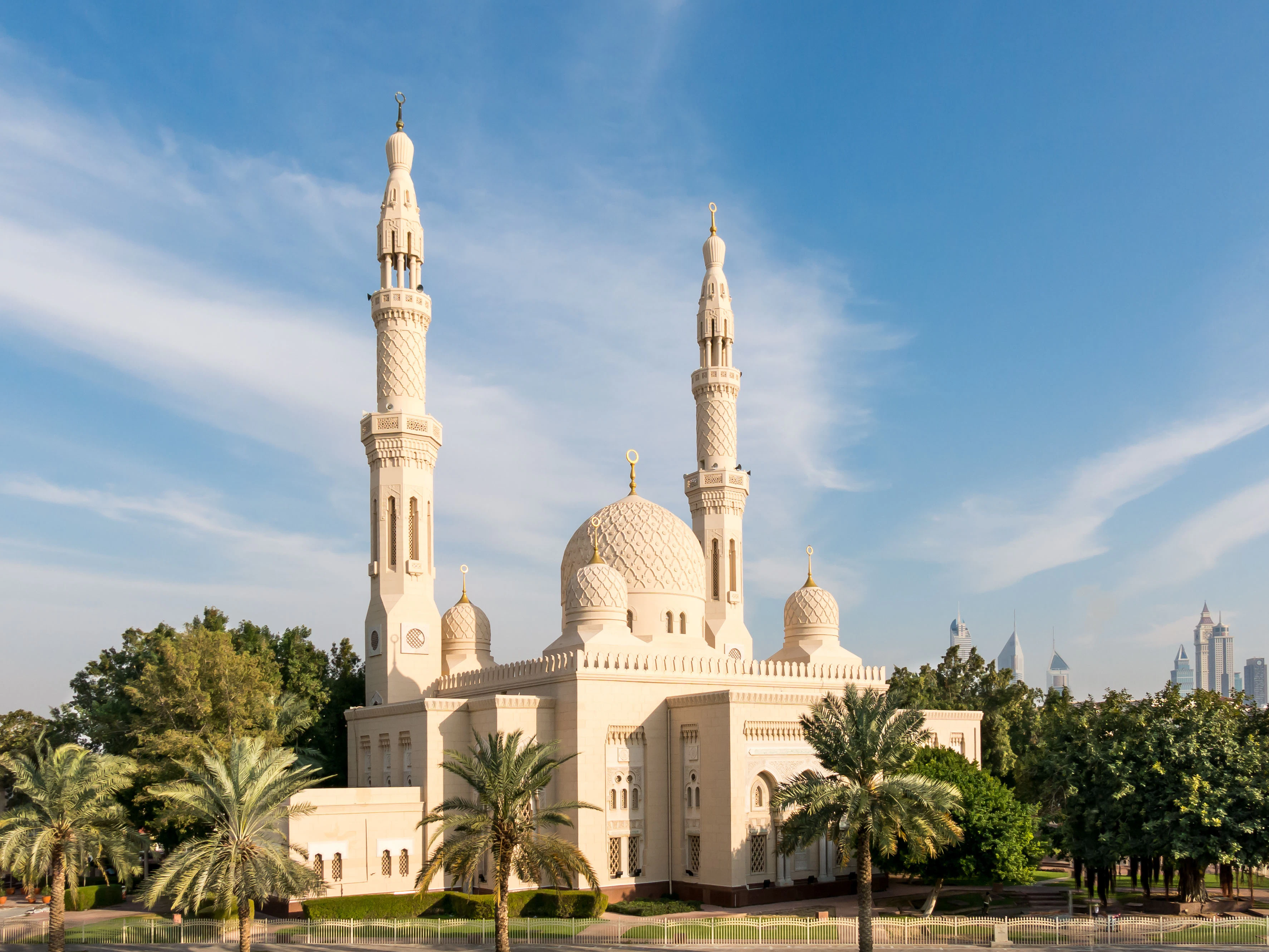 Jumeirah Mosque in Dubai with palm trees and city skyline in the background.