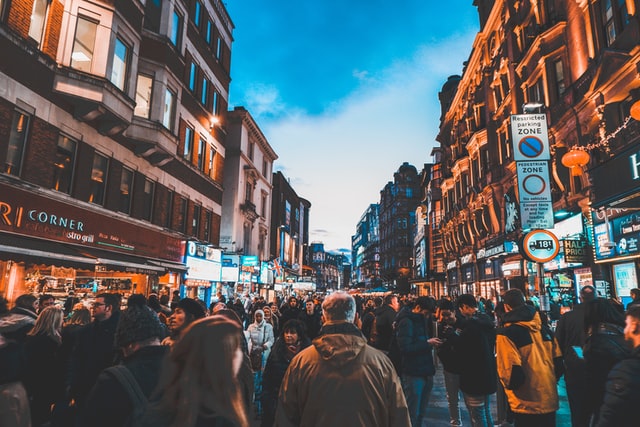 Crowded Leicester Square street scene in London with illuminated signs and historic buildings.