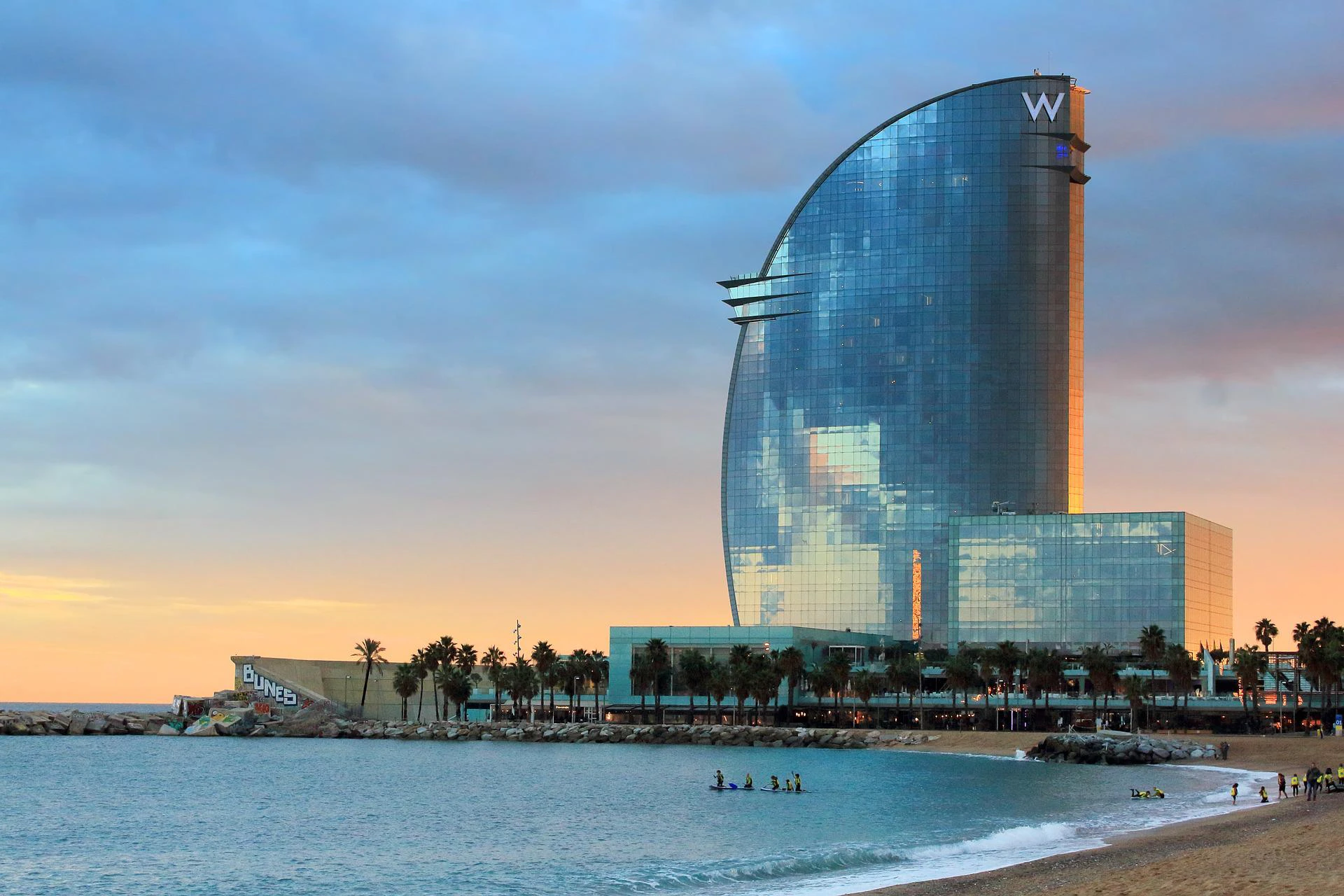 W Barcelona hotel by the beach at sunset with paddleboarders in the water.