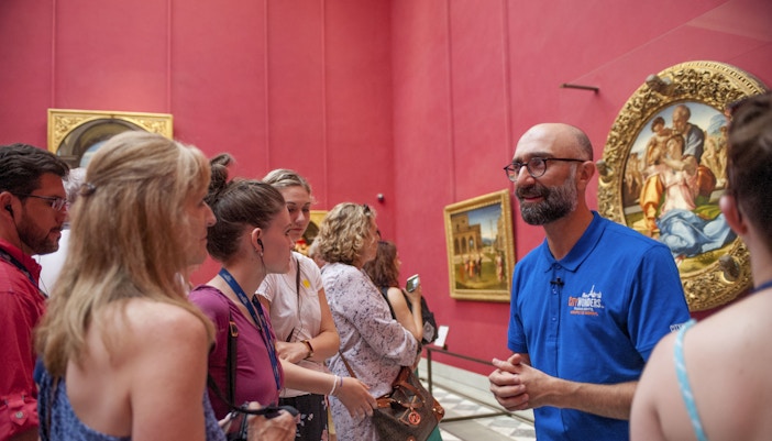 A knowledgeable guide engaging with a group of attentive tourists during a guided tour in the Uffizi Gallery's vibrant red room