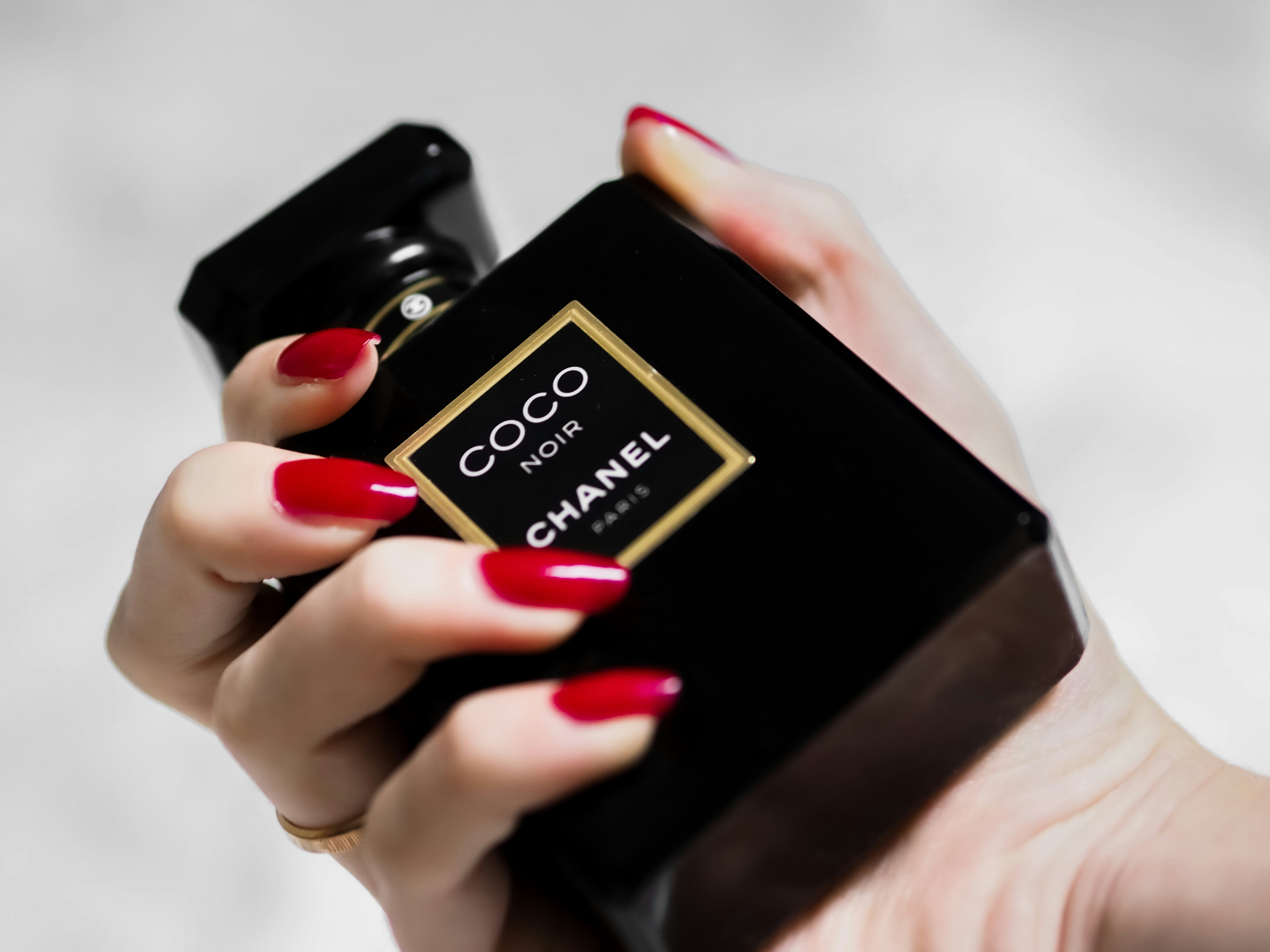 Coco Chanel Noir perfume bottle held in hand with red nails.